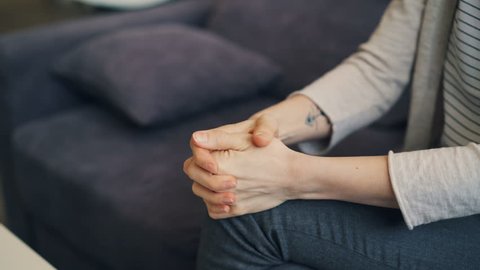Close-up of young woman moving hands expressing anxiety and nervous strain. Worried girl is sitting on sofa scratching palms with worry and hopelessness.