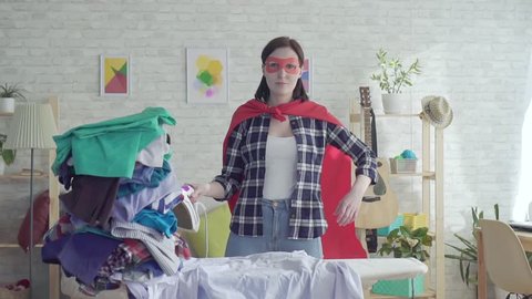 Woman housewife superhero with the iron in hand next to an Ironing board slow mo