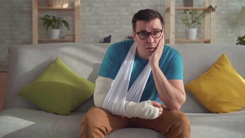 Sad young man in glasses with broken arm