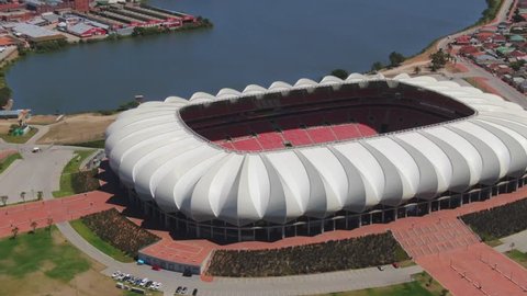 Port Elizabeth, South Africa - circa 2010s: Nelson Mandela Bay Stadium from above, turning around to see the surrounding grass park area with lake and palm trees
