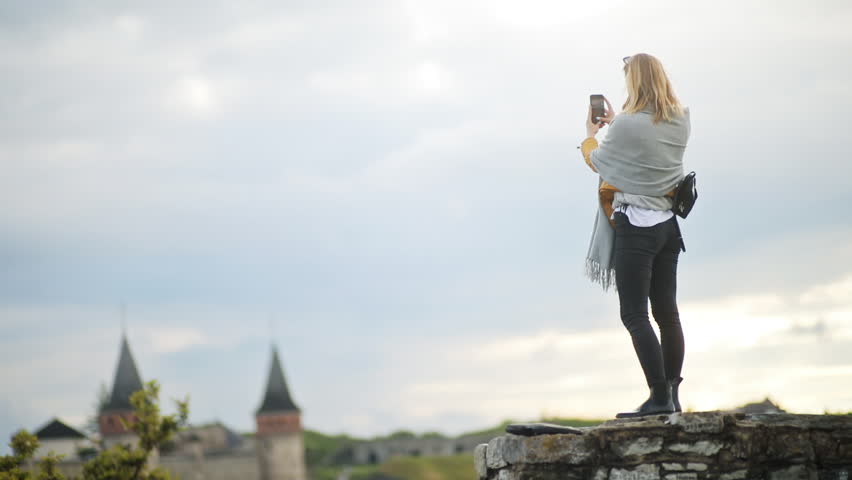 Beautiful female tourist taking photographs of the gorgeous fortress and green landscape. Summertime.