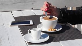 young woman in black leather jacket stirring coffee with a teaspoon in an outdoor cafe on sunny day. hand closeup