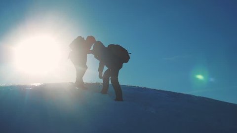 teamwork tourists winter snow business travel trip lends a helping hand. two men with backpacks hiking help each other silhouette in mountains lifestyle with sunlight. slow motion video. rock climbers