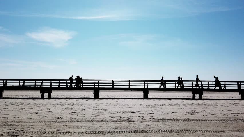 unrecognizable group of people in silhouette walking on walkway or bridge across beach at German seaside resort St. Peter-Ording