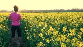 4K video clip of beautiful healthy mixed race African American girl teenager female young woman running or jogging and drinking a bottle of water in field of yellow flowers