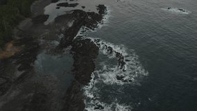 View from a drone as it ascends over a remote rocky shoreline on Northern Vancouver Island, camera tilts up revealing mountains and ocean.