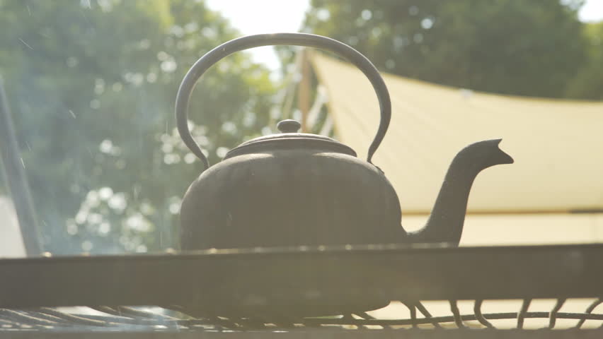 Idyllic old camping scene. Tea pot kettle boiling over open fire with tent in the background. Close up.