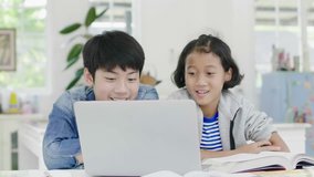 Slow motion of Young asian boy and girl watching on laptop computer at home. Children are playing online game on a laptop computer together. 