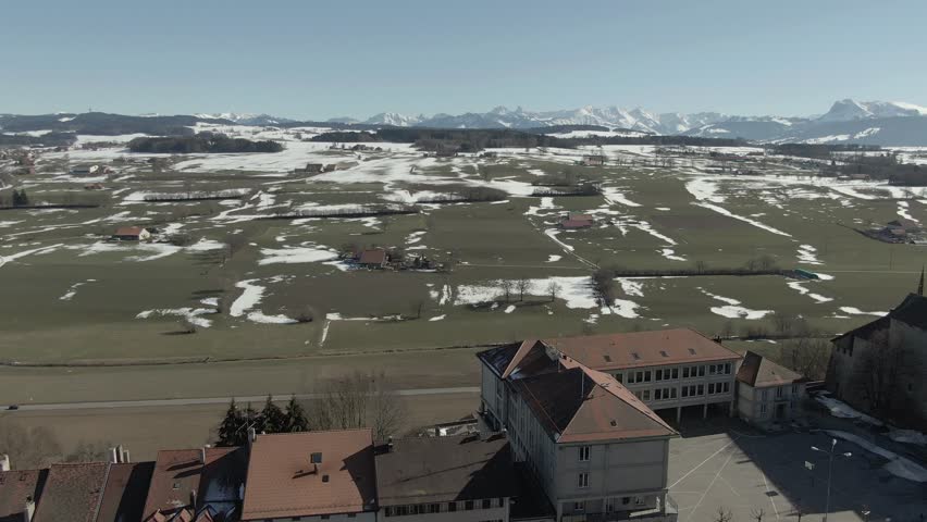 Wide aerial view flying backward over the old town Romont with snowy mountains in the background - Switzerland.