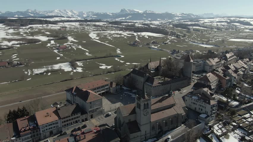 Wide aerial high drone shot circling over the Swiss town Romont with white snowy mountains in the background.