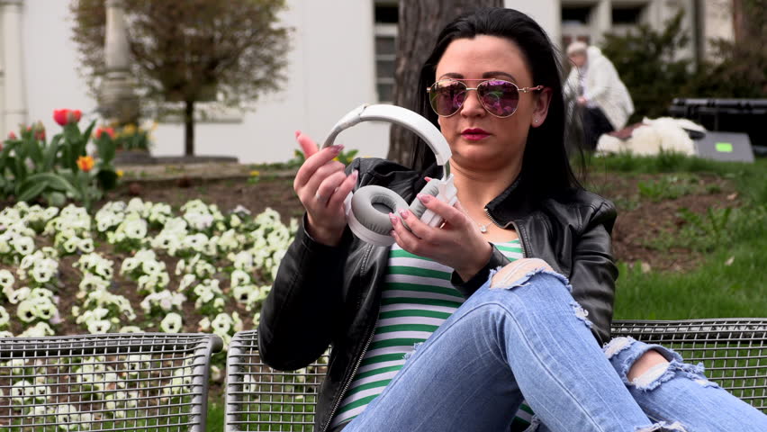 Brunette sits on a street bench and listens to music