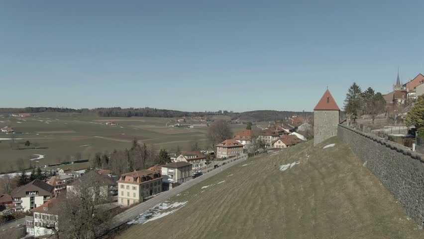 Wide aerial shot flying over a slope and past an old rampart in Romont Switzerland.
