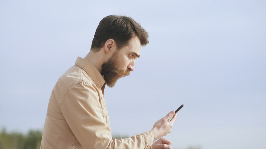 Surprised man holding smartphone and lookinf at it. Outdoors.