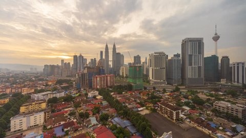 Aerial cloudy sunrise view of Kuala Lumpur city skyline with busy streets at an old village at dawn in Federal Territory, Malaysia. Pan up motion timelapse.