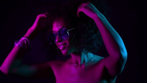 Portrait of sexy woman with afro hair in neon purple light having fun smiling and dancing in studio against black background. slow motion.