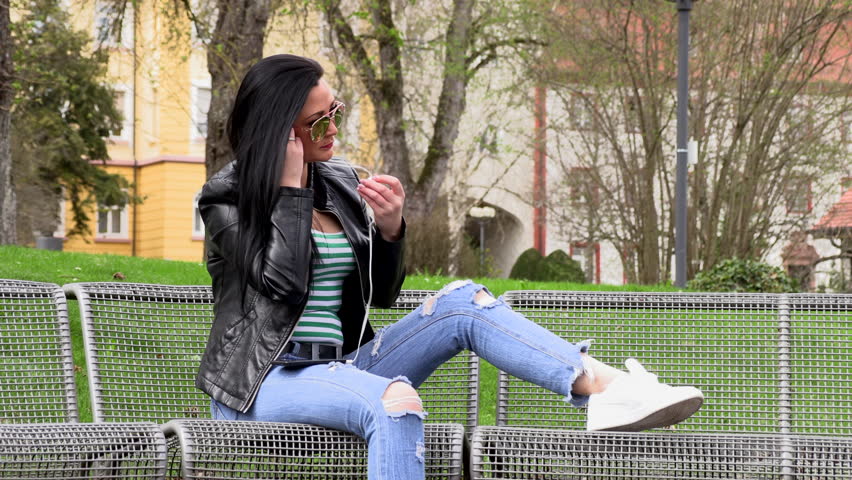 Brunette sits on a street bench and listens to music