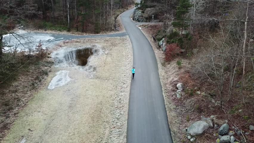 Arial drone view of a guy running on a country road in the winter