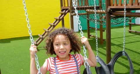 Front view close up of mixed-race schoolgirl playing on a swing at school playground. She is smiling and looking away