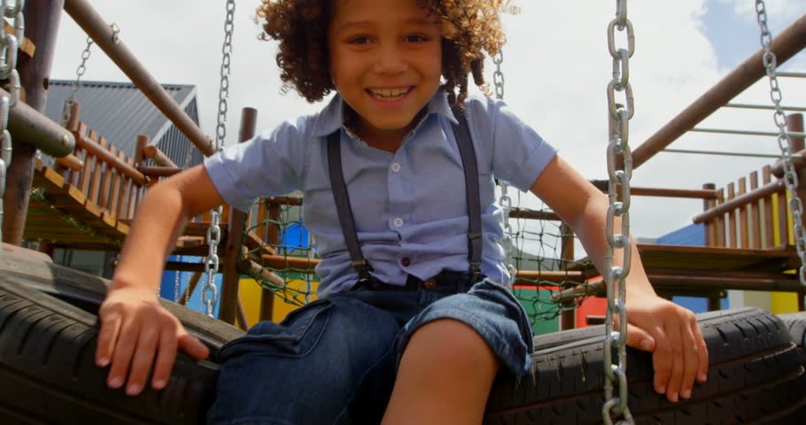 Front view close up of mixed-race schoolgirl playing on hanging tyre in the school playground. She is smiling and looking at camera 