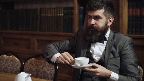 Luxury lifestyle, success, elegance, tea time concept. Aristocrat sits in luxury interior and drinks tea or coffee. Bearded man in elegant suit in his cabinet. Rich man with calm face enjoys tea time