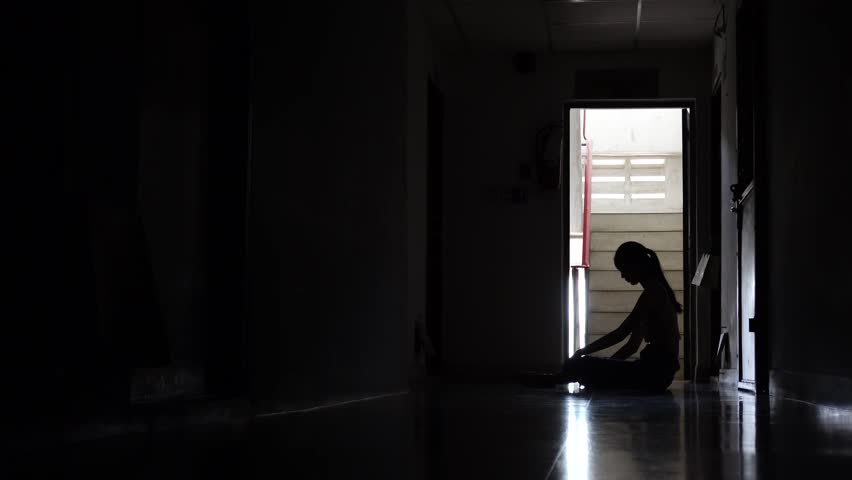 Silhouette of a sad young girl sitting in the dark leaning against the wall in old condo, Domestic violence, family problems, Stress, violence, The concept of depression and suicide.