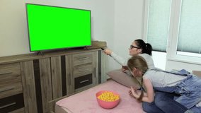 Daughter and mother using remote control near TV with green screen
