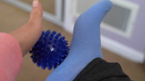 Woman with plantar fasciitis uses a spiky ball to massage her aching foot and heel