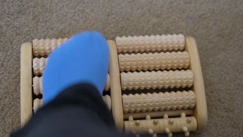 Woman with plantar fasciitis uses a wooden foot roller with spikes to massage her aching foot
