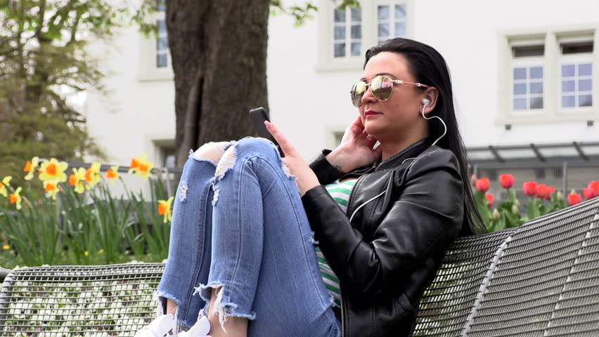 Brunette sits on a street bench and listens to music