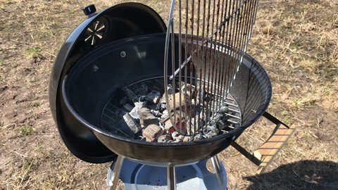 Burning coals and wood on a grill grate. Preparation of coal for barbecue in a large round open grill. The concept of relaxation and enjoyment of food. Man puts the meat grill