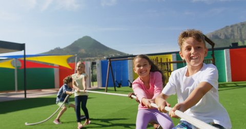Front view of mixed-race schoolkids playing tug-of-war in the school playground. They are having fun together 