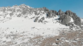 Travel in winter: man mountaineering in winter mountains,  aerial video. Drone flight mountain landscape, man backpacker hiking sunny day. Tourism, nature and trekking concepts. 