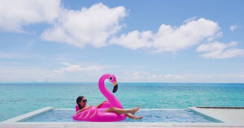 Summer Vacation Woman in bikini on inflatable pink flamingo pool toy mattress in swimming pool. Elegant lady relaxing sunbathing enjoying travel holidays at resort pool. Luxury lifestyle.