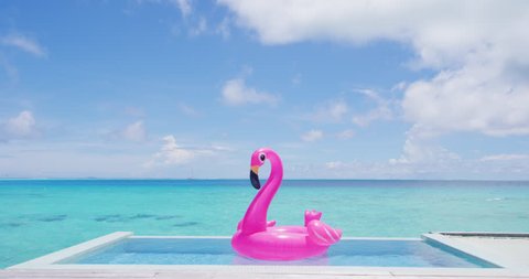 Vacation travel concept with inflatable pink flamingo float toy mattress in luxury swimming pool. Luxury lifestyle summer holidays travel background video.