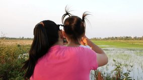 Asian young woman and daughter use smartphone take a video of Rice seedlings in cultivation plots with sunset background.