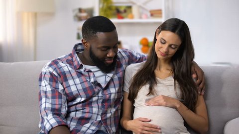 Mixed-race family looking at camera, pregnant woman holding tummy, happiness