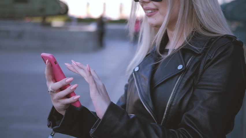 Smiling blonde woman browsing smartphone. Slider shot of hands with trendy coral pink manicure. Social networking.