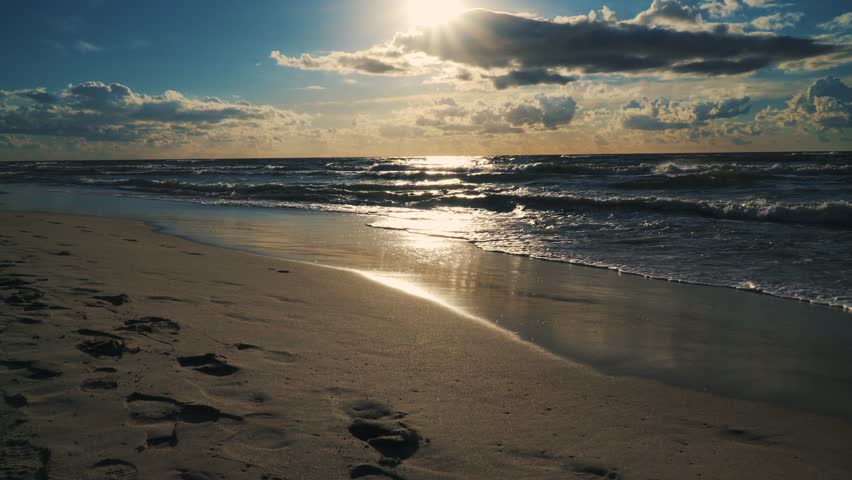 sunset behind clouds over sea waves and sandy beach in summer