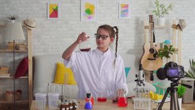 portrait of a teenage girl video blogger in a white coat and goggles in the lab looking at the camera smiling