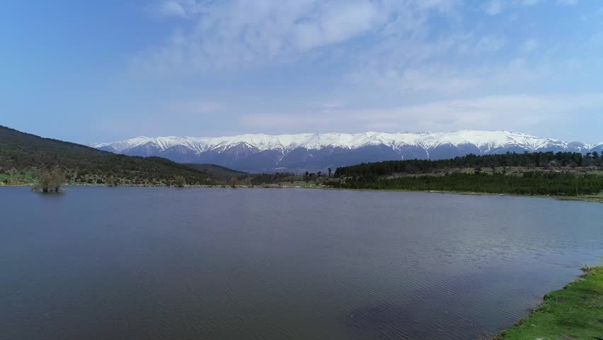 Lake Snowy Mountains with  Blue Sky, Clouds drone flight towards snowy mountain landscape with green vegetation over the lake