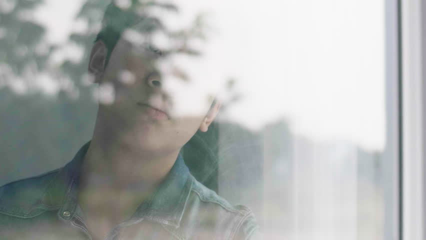 Asian boy is sad looking out the window, The boy face close up child through the glass. Sad boy looks out the window. 60fps Royalty-Free Stock Footage #1028344352
