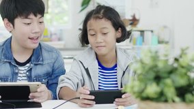 At Home Sitting on a table: Cute Little Girl and young Boy Playing in Competitive Video Game on  Smartphones and tablet, Holding them in Horizontal Landscape Mode. 60fps in dolly Shot.