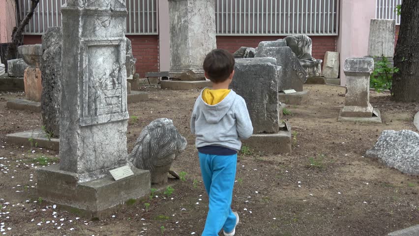 Fethiye Archaeological Museum, Fethiye, Turkey - 8th of April 2019: 4K Sad and curious child wanders between stele and obelisks
