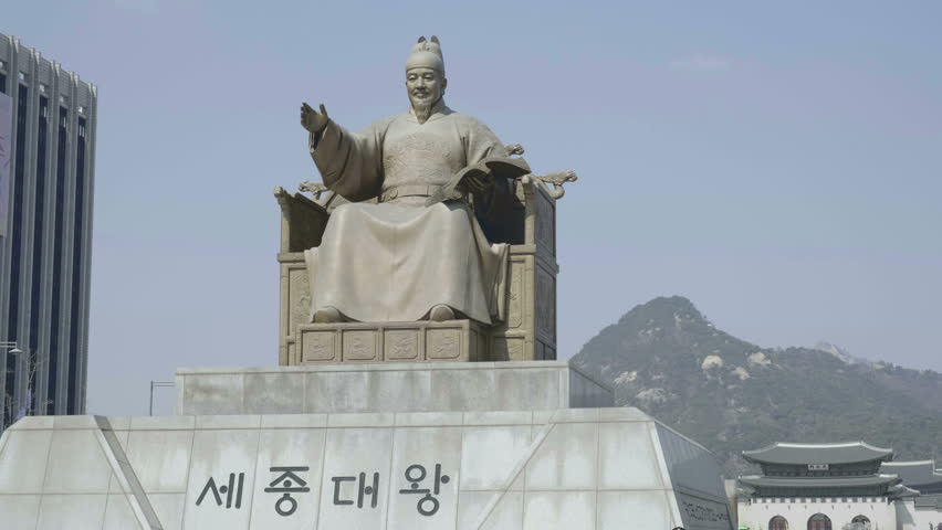 Camera orbiting left tracking the front of King Sejong the Great statue and base with mountain background in downtown Seoul city center, South Korea (Korean text translated, Sae Jong Dae King)