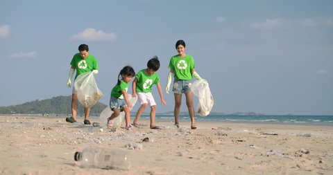Group of volunteers in green t-shirts cleaning up the beach with plastic bags full of garbage. Slow Motion. Safe ecology concept. 4k resolution.
