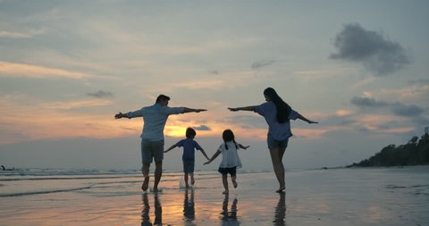 Silhouetted happy asian family playing and having fun on the beach at sunset. Slow Motion. Family, Freedom and Travel concept.