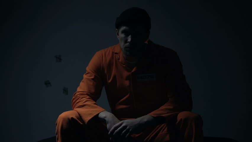 Prisoner sitting in cell while light blinking, unwilling to participate in riot