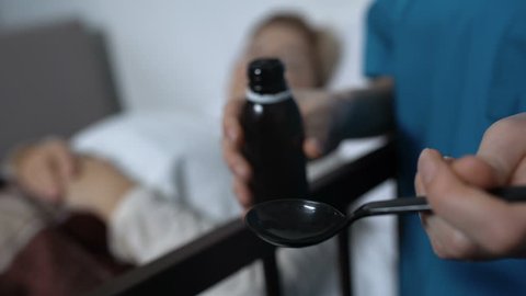 Doctor assistant giving sedative syrup to female patient, care in nursing home