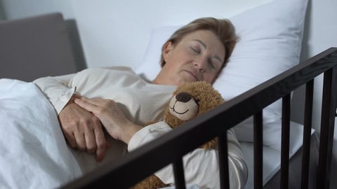 Caring nurse covering female patient who sleeping with teddy-bear with blanket