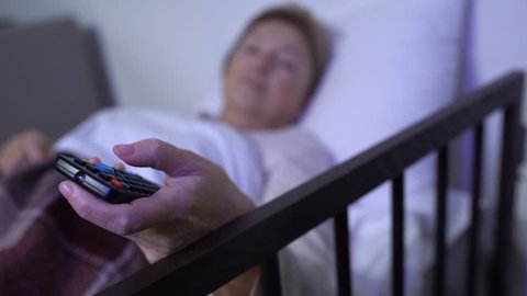 Woman lying on sickbed and switching channels on tv, personal ward in hospital